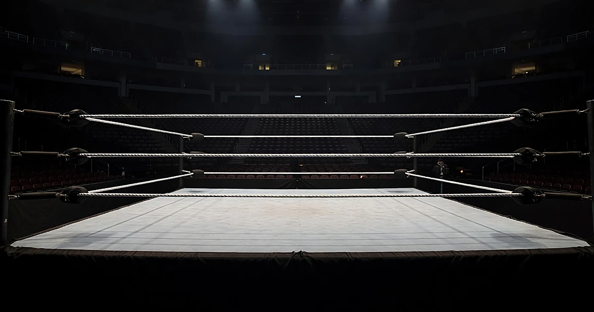 Empty professional wrestling ring under spotlights in darkened arena with vacant seating in background