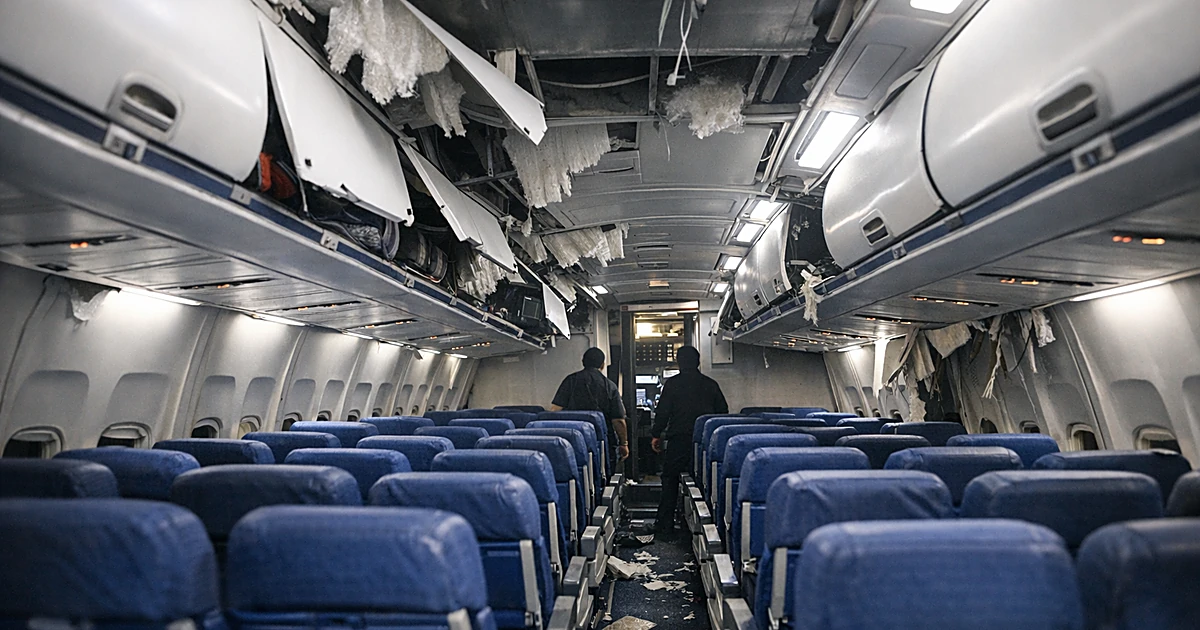 Interior of commercial aircraft cabin showing damaged overhead panels and exposed ceiling structure