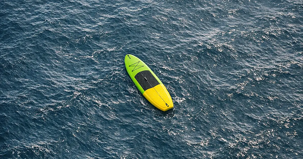 Empty paddleboard floating alone on open ocean water with current ripples