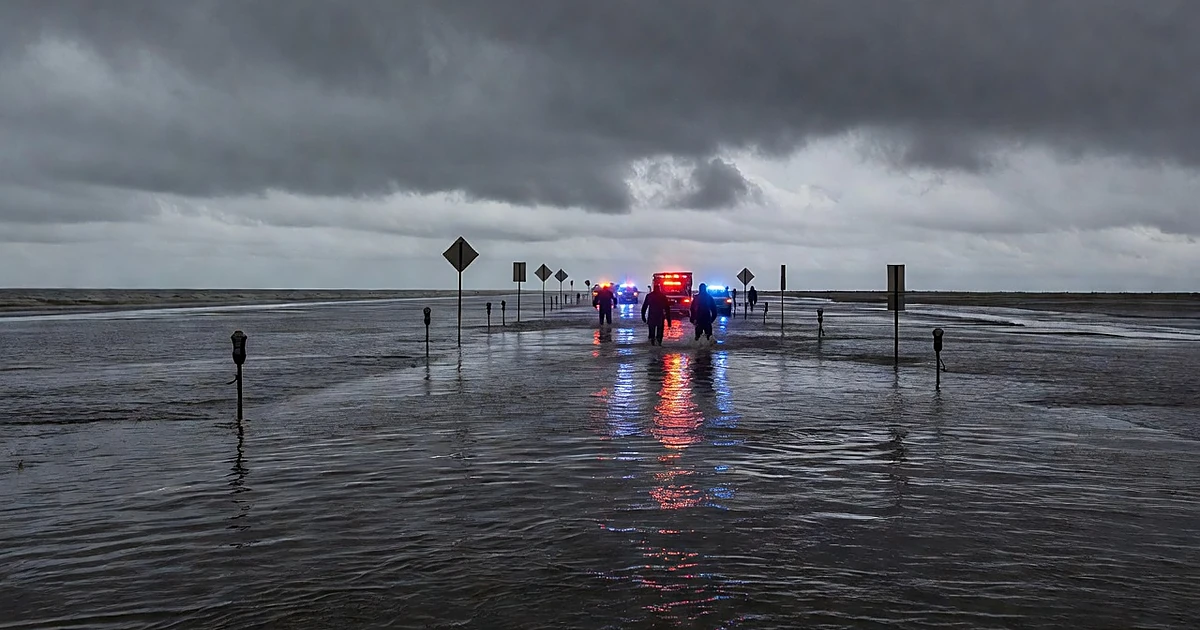 Flooded street with emergency responders wading through deep water under stormy skies with vehicle lights reflecting
