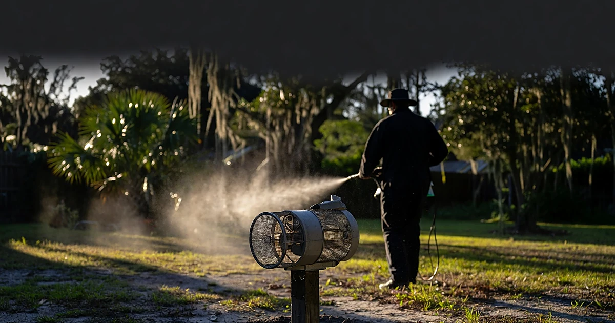 Mosquito trap device in Florida yard with public health worker fogging in background at sunset