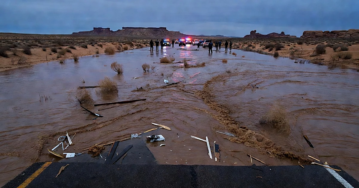 Floodwater rushing across desert highway with emergency vehicles and flashing lights at dusk