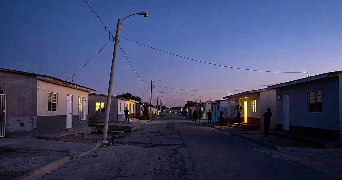 Residential street at dusk with cracked pavement and homes with lit windows in Caribbean neighborhood