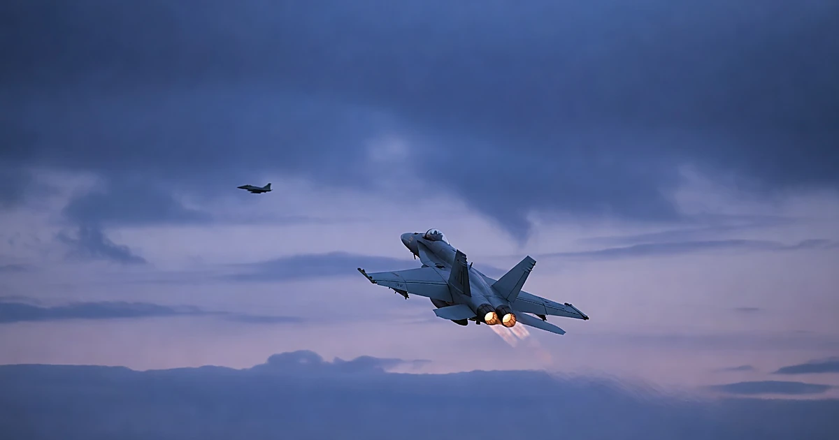 Fighter jet climbing through dusk clouds over Baltic Sea with afterburners glowing