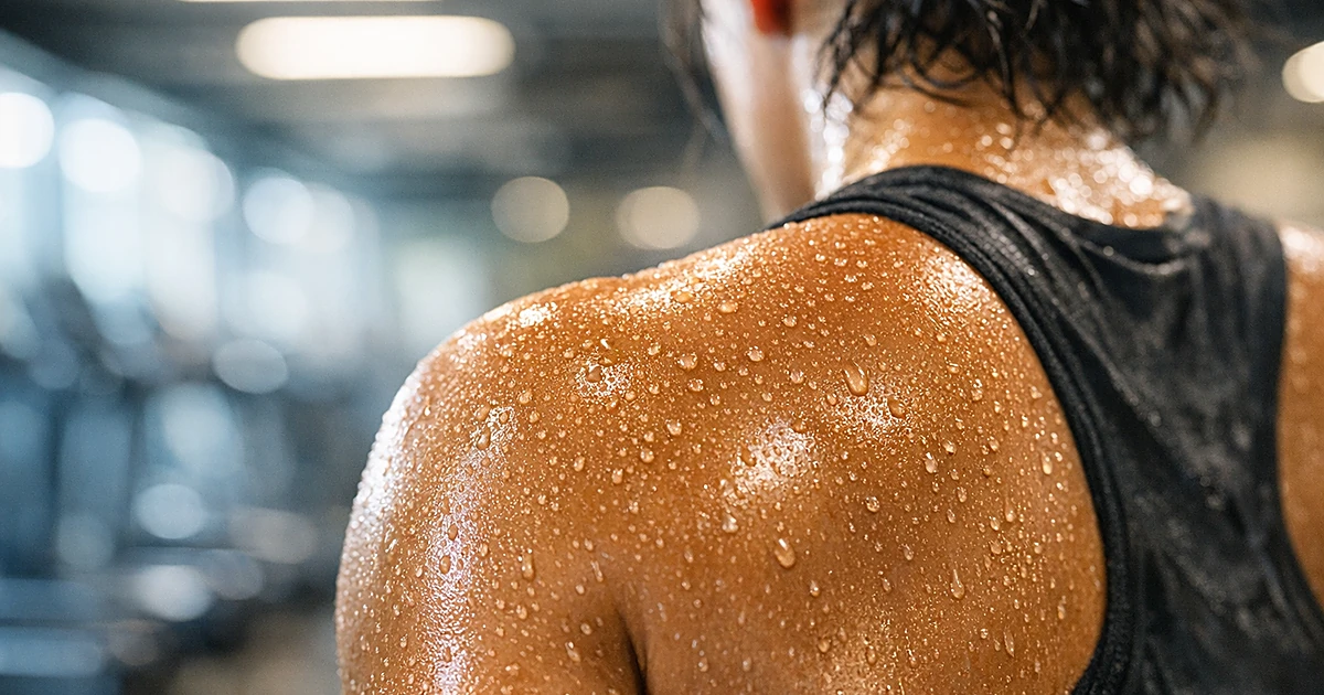 Close-up of perspiration beads on a person's shoulder in a gym setting with blurred equipment in background