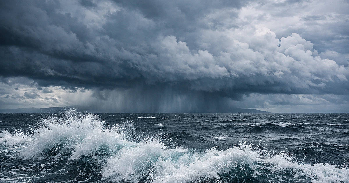 Dark storm clouds and heavy rain approaching over churning Pacific Ocean waters with crashing waves