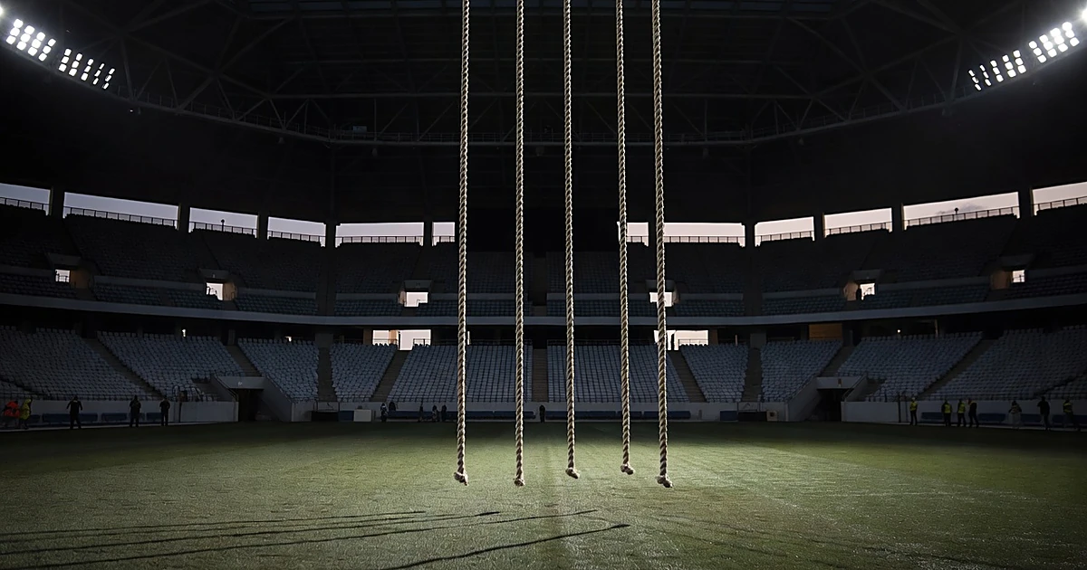 Four rappelling ropes hanging from indoor stadium ceiling above empty turf field at dusk