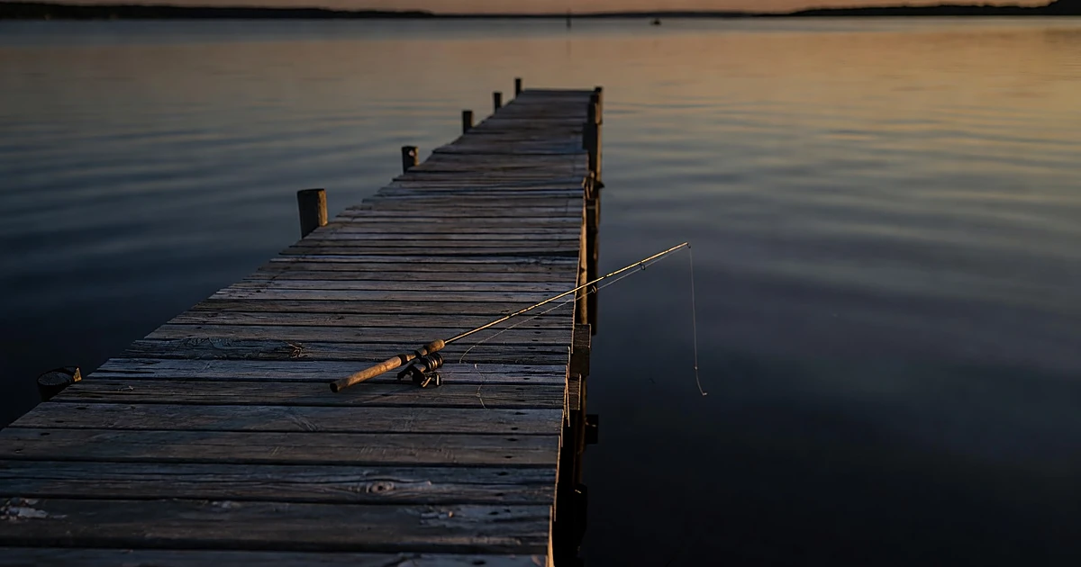 Abandoned fishing rod on wooden dock extending into dark water at dusk