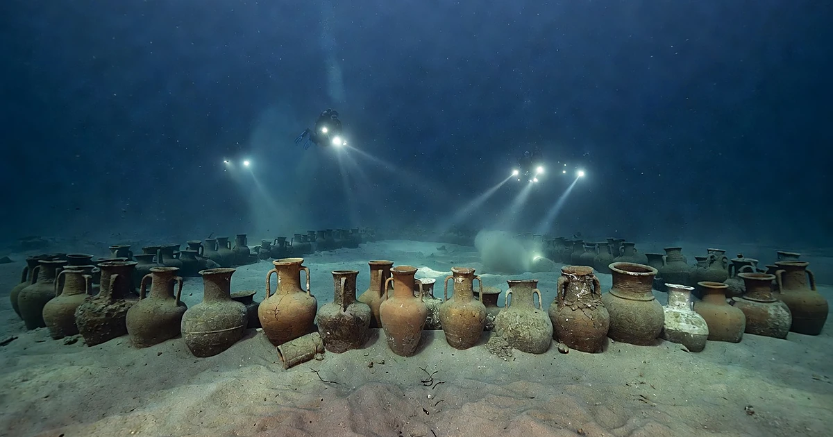 Ancient ceramic amphorae and stone anchors on Mediterranean seabed illuminated by diving lights underwater