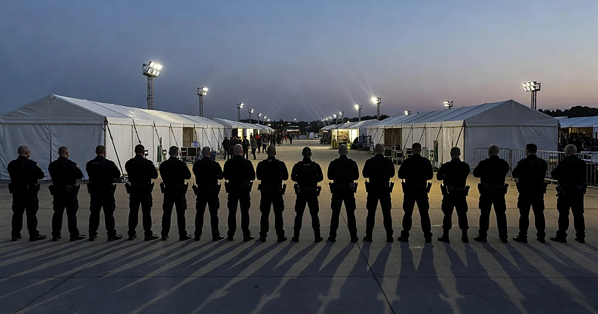 Security personnel silhouettes standing guard at outdoor festival grounds with vendor tents at dusk