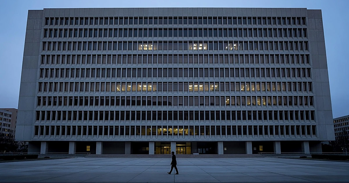 Lone silhouetted figure walking toward massive brutalist government building at dusk with glowing windows