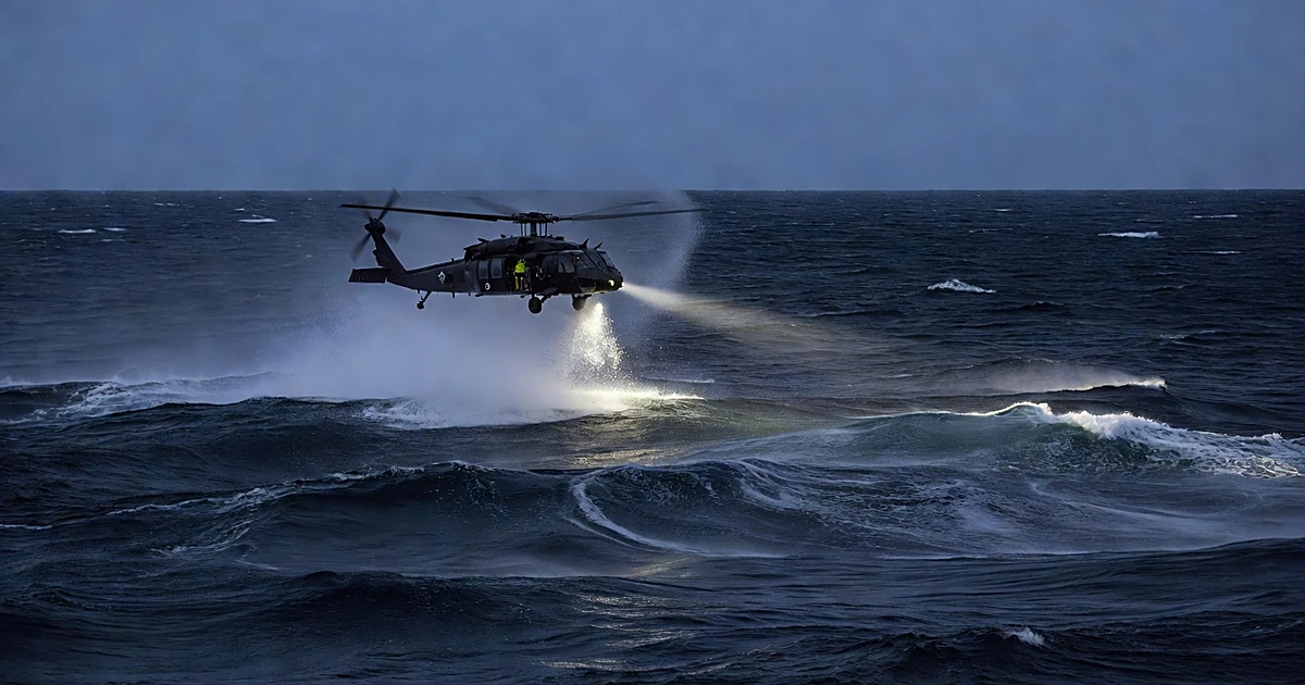 Coast Guard helicopter searching over dark ocean waters at dusk with searchlight beam cutting through spray