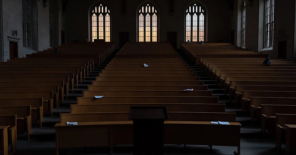 Empty university lecture hall with podium silhouetted against gothic windows at dusk