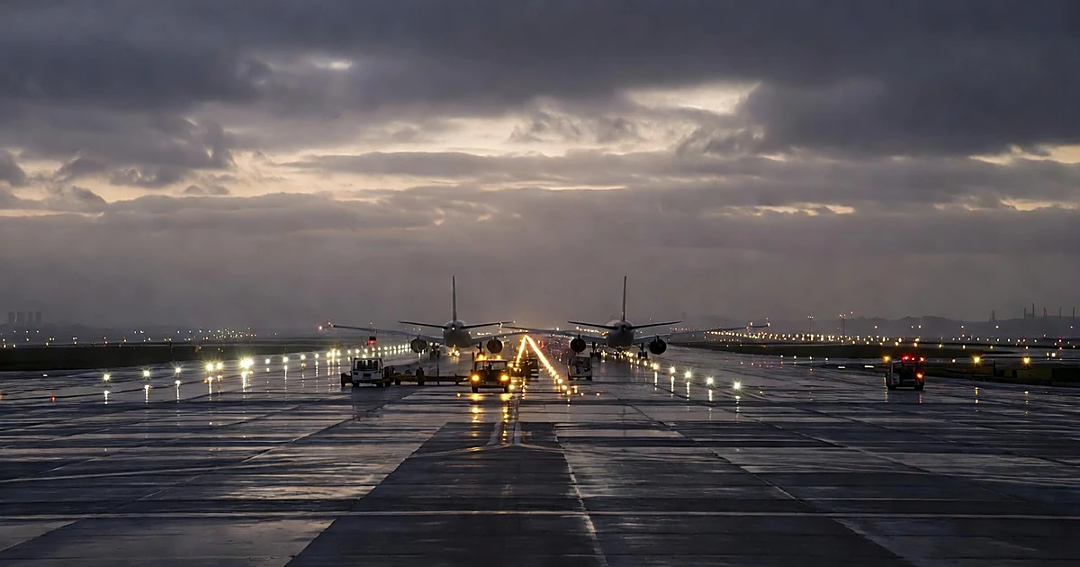 Two commercial aircraft silhouettes positioned close together on wet airport tarmac at dusk with runway lights