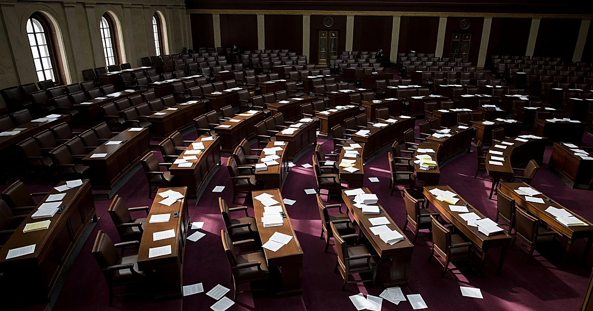 Empty congressional chamber with scattered papers on desks suggesting political division and debate