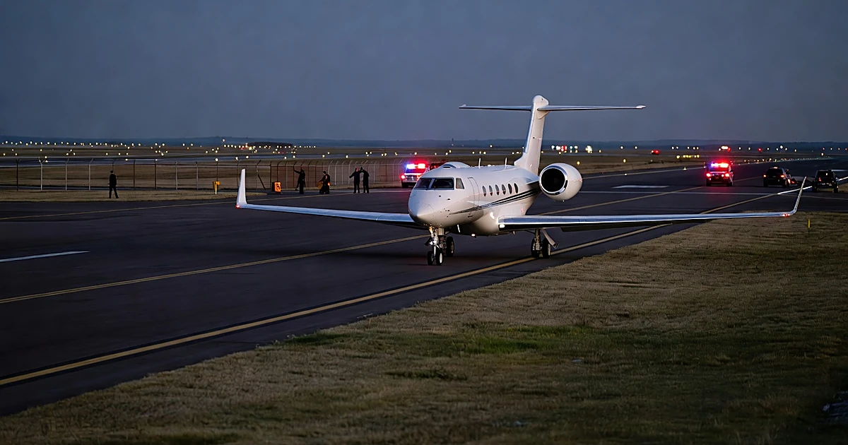 Private jet on airport runway at dusk with perimeter fencing and emergency lights in background
