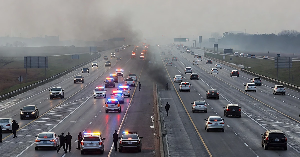 Interstate highway with emergency vehicle lights flashing and smoke rising from roadway as silhouetted responders work
