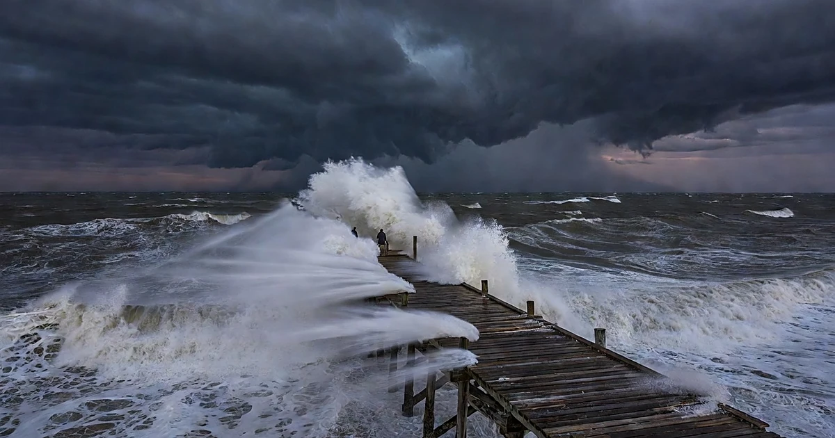 Storm system over turbulent ocean waters with waves crashing against coastal pier at dusk