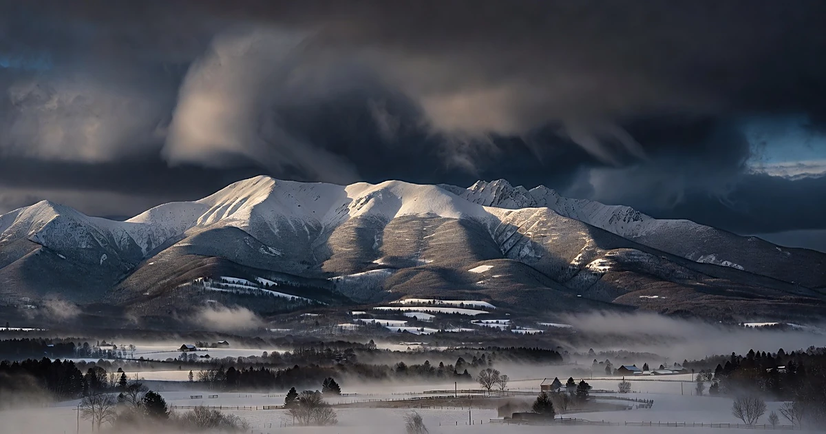 Snow-covered Appalachian mountain ridge under gathering storm clouds at dusk with rural valley below