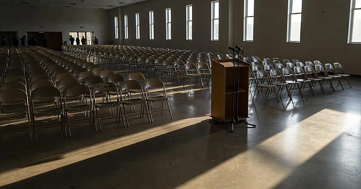 Empty community hall with rows of chairs facing podium, sunlight streaming through windows creating shadows