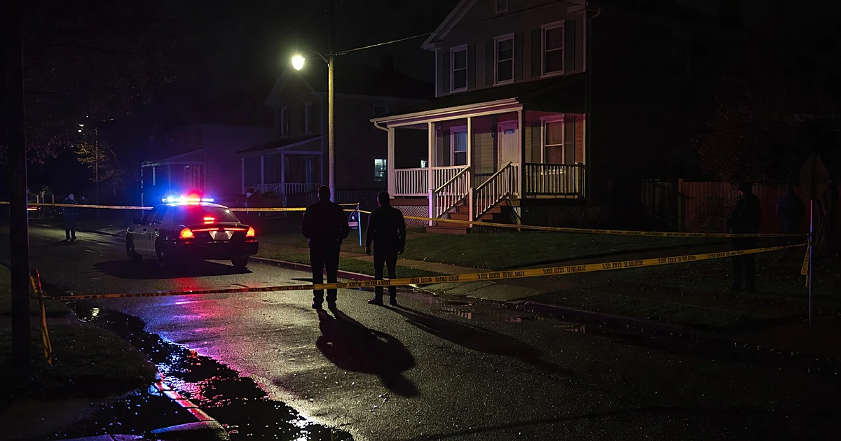 Police emergency lights illuminate a residential home at night with crime scene tape in foreground