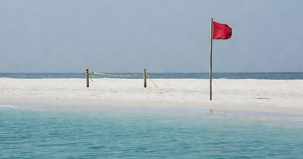 Empty tropical beach with red warning flag and yellow caution tape blocking access to turquoise water