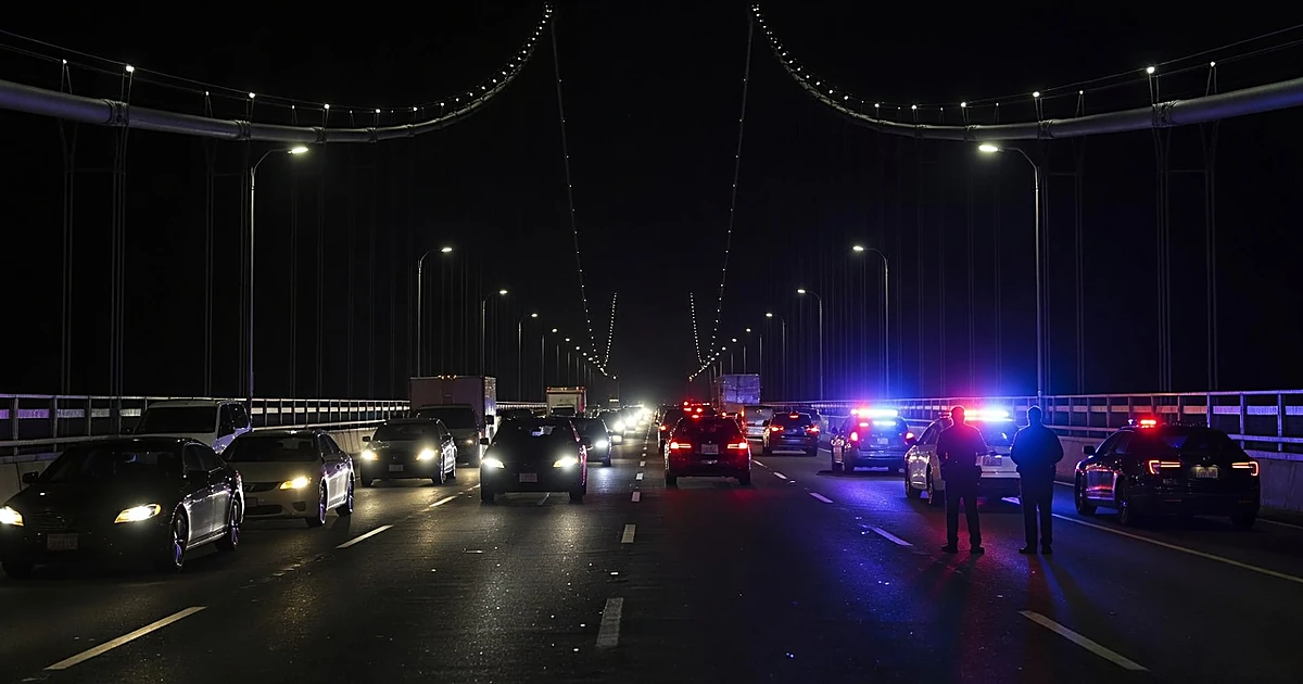 Police lights flashing on George Washington Bridge roadway at night with traffic and officers investigating