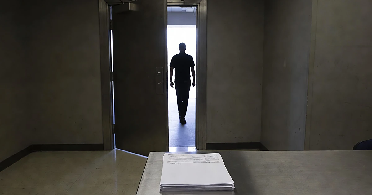 Open security door in county booking station with silhouetted figure walking toward exterior light