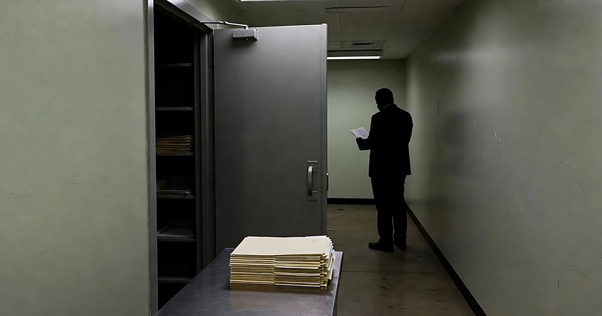 Evidence locker door ajar in county courthouse room with case folders on examination table and silhouetted figure