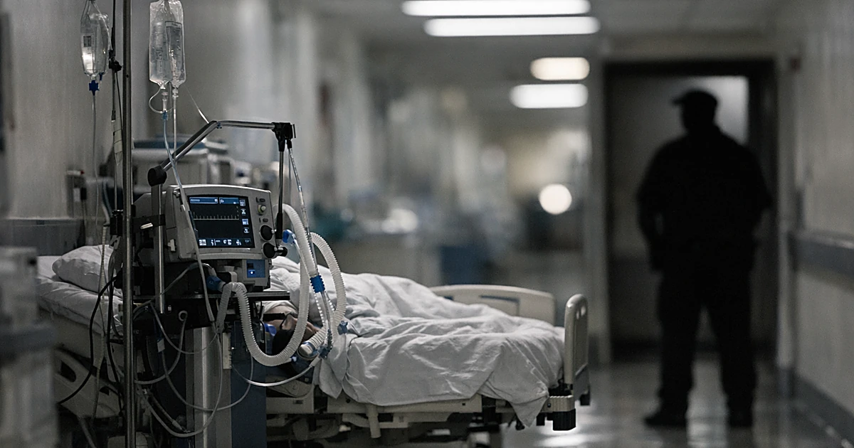 Hospital corridor with ventilator beside occupied bed and guard silhouette in doorway under fluorescent lighting