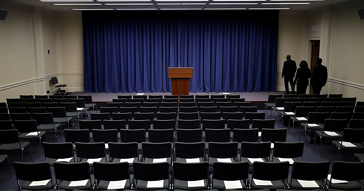 Empty White House press briefing room podium with blue backdrop and vacant press chairs in foreground