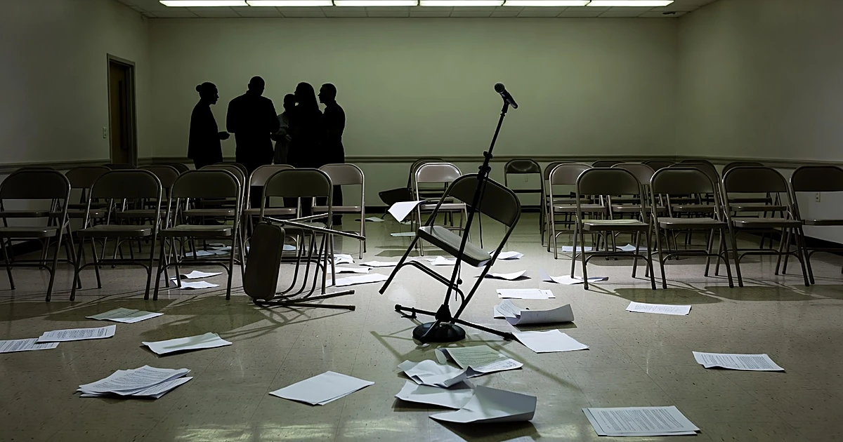 Community meeting room with scattered chairs and papers after contentious public housing discussion
