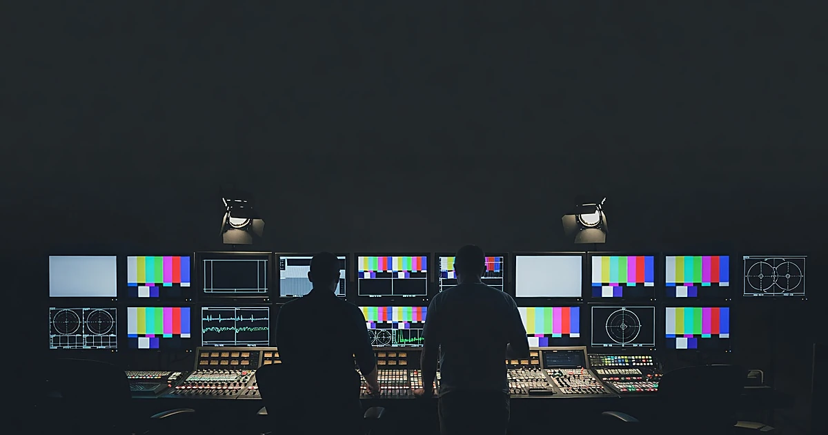Television production control room with silhouetted crew members at mixing console reviewing monitors