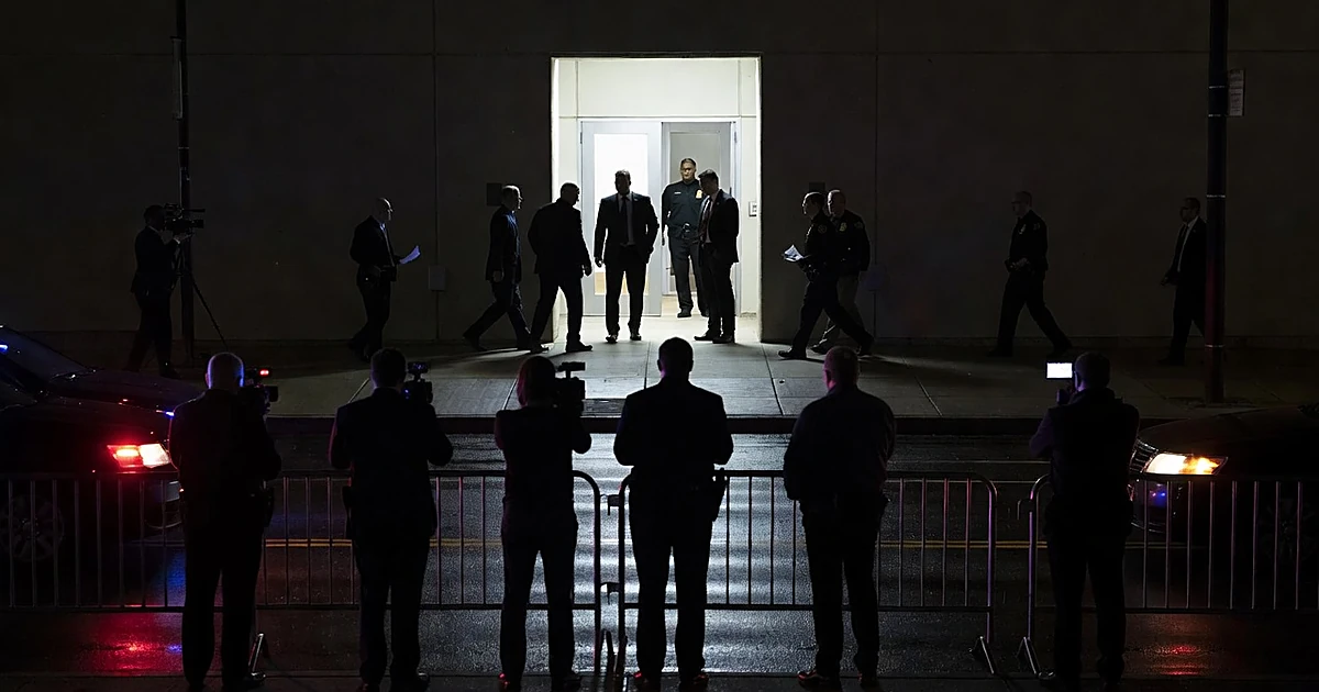 Federal immigration enforcement facility entrance at night with silhouetted figures and emergency lights