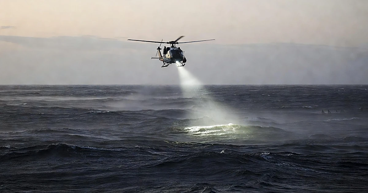 Coast Guard helicopter with searchlight scanning dark ocean waters during dawn search and rescue operation