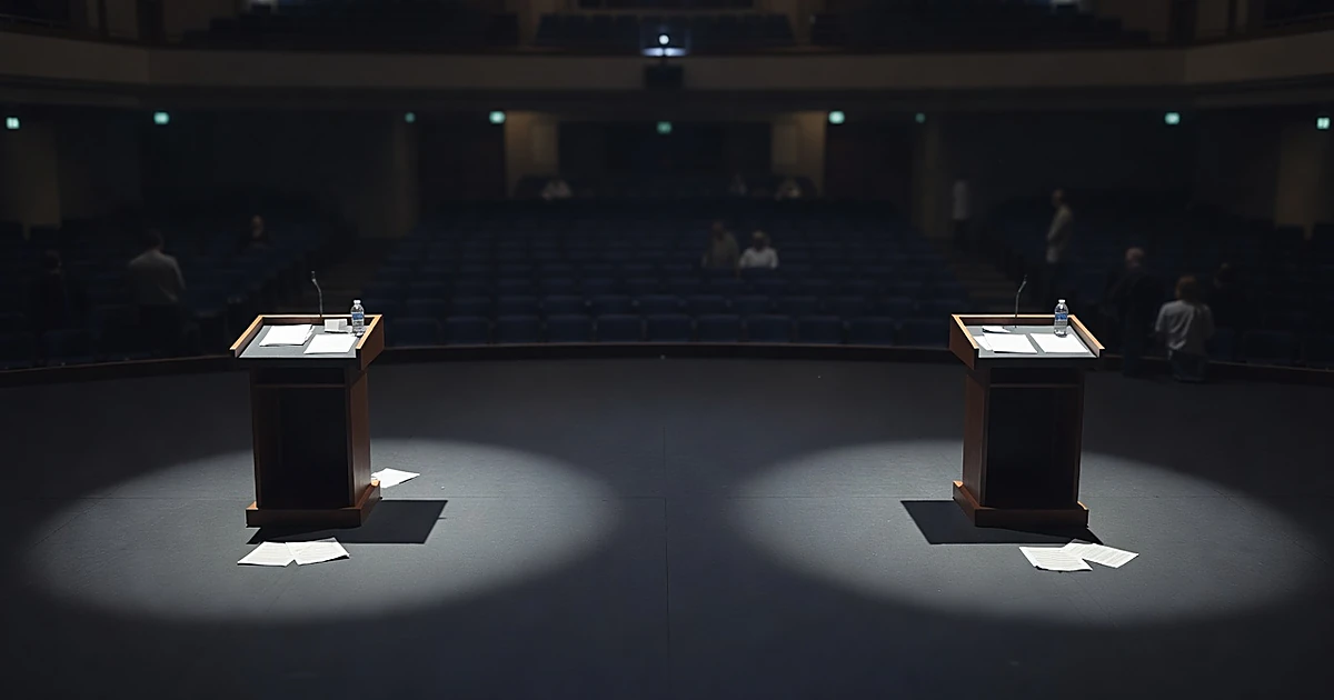 Empty debate stage with two podiums separated by distance under dramatic spotlights in Grand Rapids auditorium