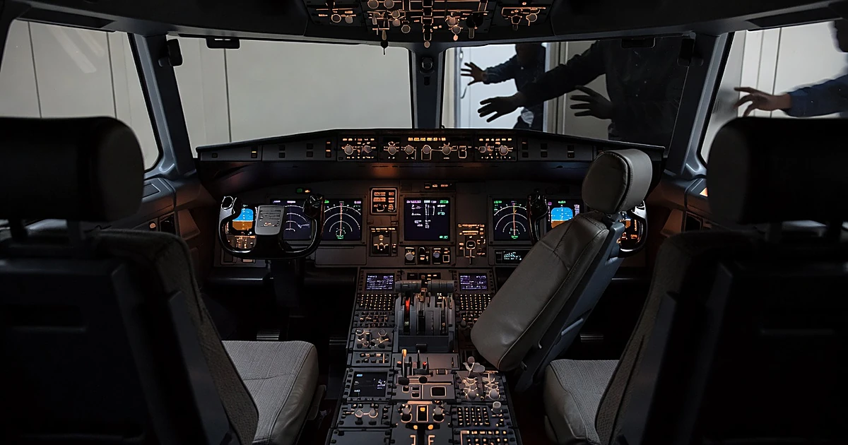 Empty aircraft cockpit with instrument panel glowing and silhouetted crew members reaching forward from doorway