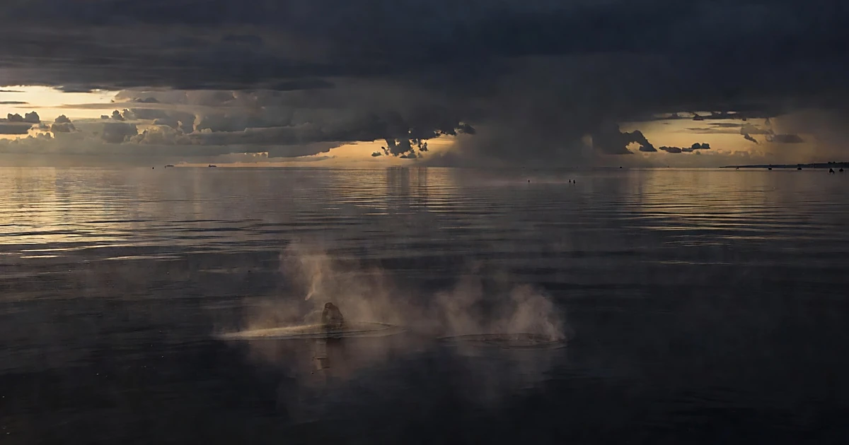 Wide view of Pacific Ocean at dusk with steam rising from warm water surface under gathering storm clouds