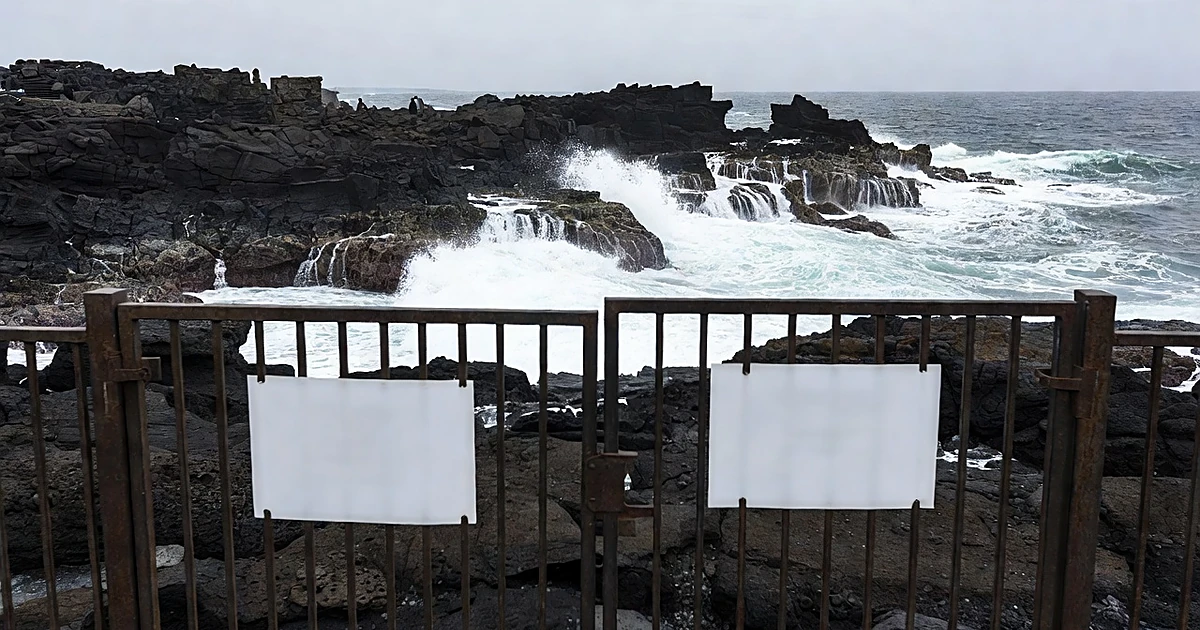 Locked gate with chain partially open leading to black sand volcanic coastline with ocean waves