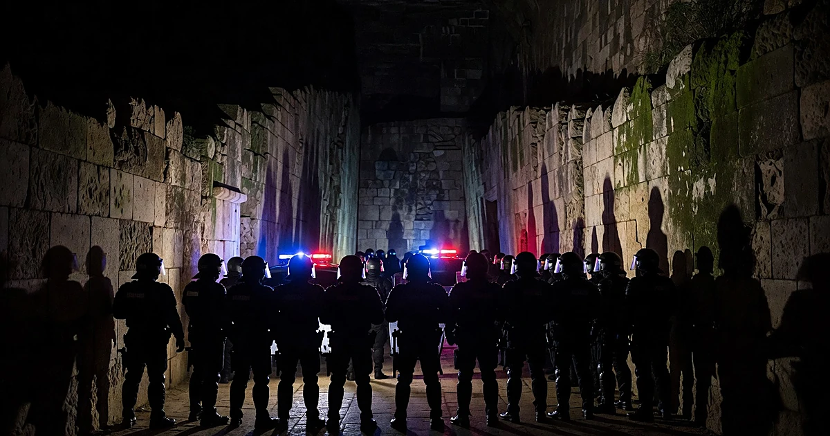 Riot police silhouettes form defensive line in ancient Roman amphitheater corridor with emergency lights flashing