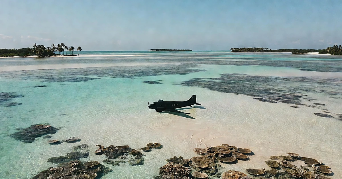 Submerged vintage aircraft silhouette in shallow Pacific lagoon water surrounded by coral and sand patterns