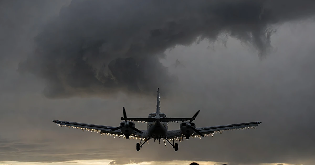 Small aircraft silhouetted against stormy winter clouds with visible ice accumulation on wings