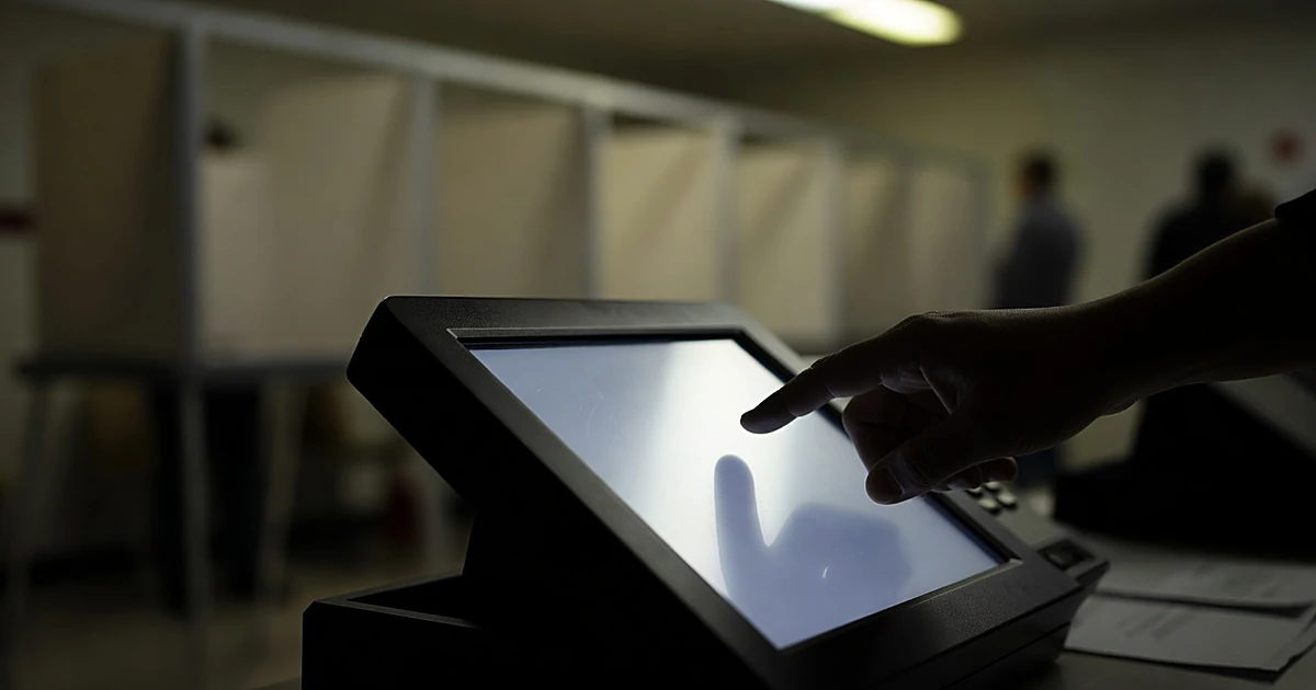 Silhouetted hand reaching toward electronic voting machine touchscreen at polling station