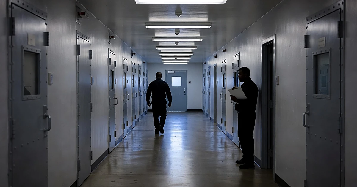 Prison corridor with silhouetted corrections staff near medical facility doors under fluorescent lighting