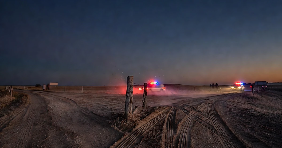 Rural road junction with tire tracks and emergency vehicle lights at dusk
