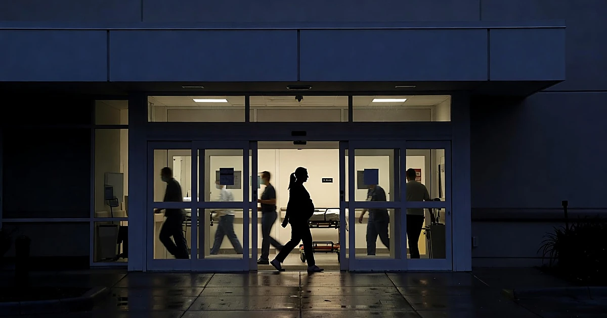 Silhouetted pregnant woman entering illuminated hospital emergency room entrance at dusk with medical staff visible inside
