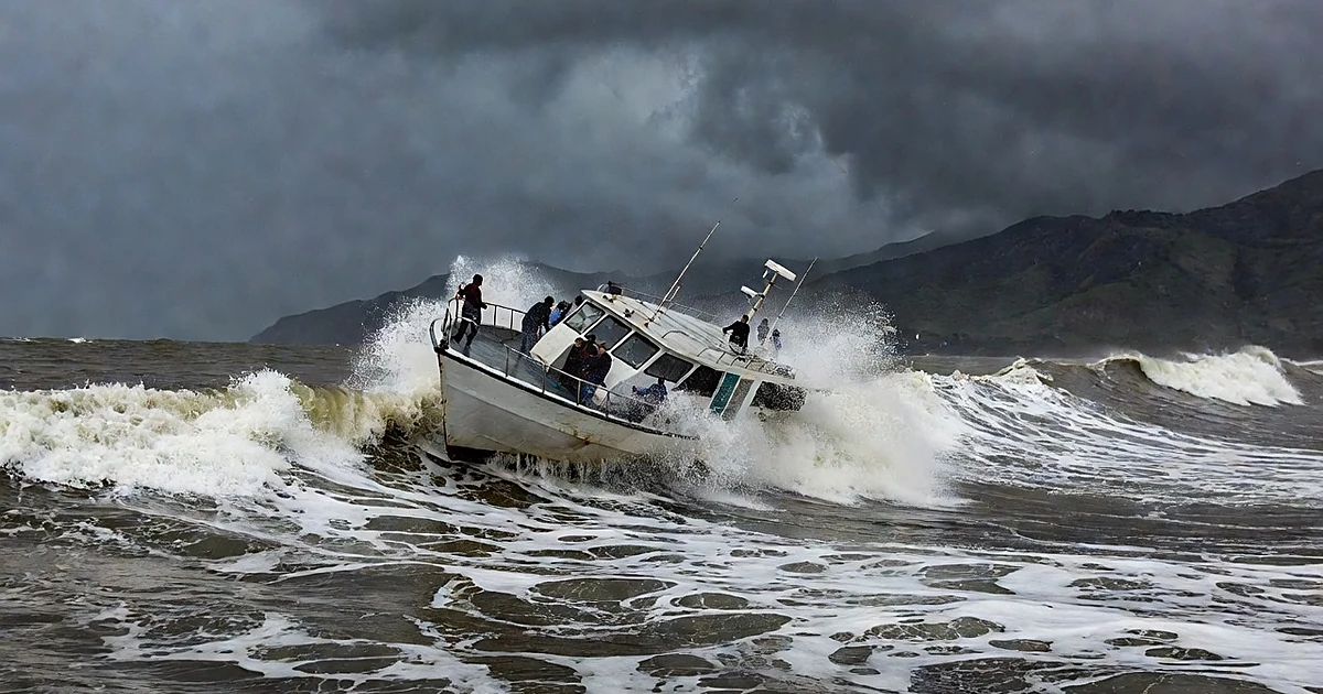 Tourist boat tilting in rough ocean waves off tropical coast with storm clouds overhead