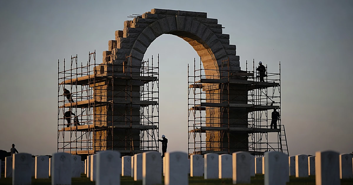 Massive stone arch under construction at dusk with military cemetery headstones in foreground