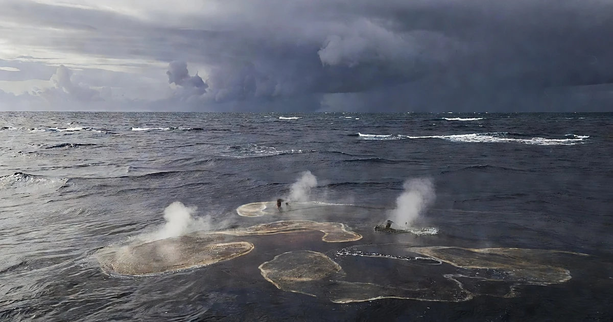 Wide view of tropical Pacific Ocean with heat shimmer rising from warm water surface under dark storm clouds
